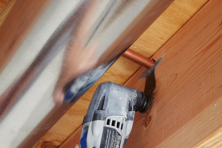 An oscillating tool cuts through copper pipe in a hard-to-reach area